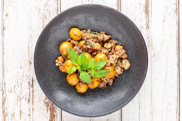 Ovo de ovário de frango frito quente e picante com miudezas de vísceras de frango arrancar variedade de carnes carnes de órgãos e manjericão em chapa escura em fundo de textura de madeira branca vista superior Comida de rua local tailandesa