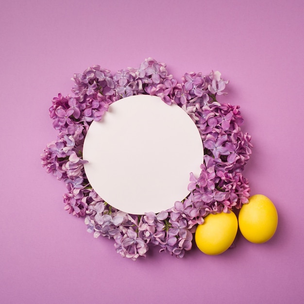 Foto ovo de páscoa amarelo e ramos de lilás sobre fundo roxo.