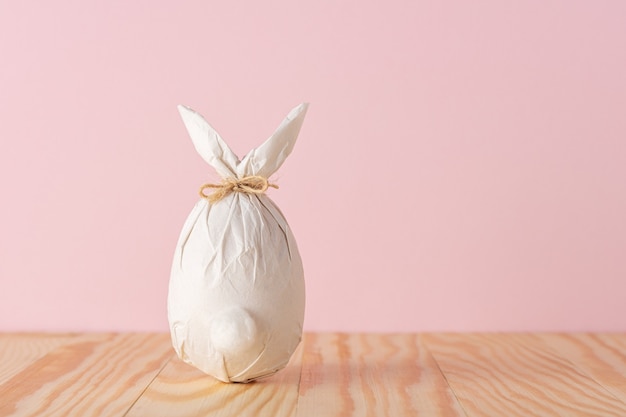 Ovo de páscoa embrulhado em um papel em forma de coelho na mesa de madeira.