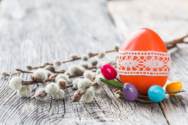 Ovo de Páscoa vermelho decorado com rendas e galho de salgueiro na mesa de madeira. Foco seletivo, cópia