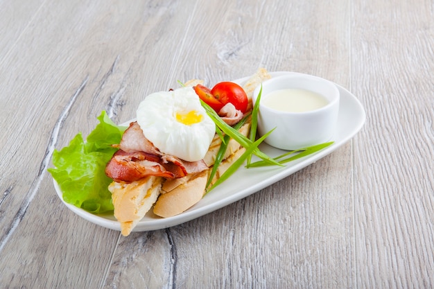 ovo escalfado com bacon, tomate cereja cebola em uma baguete e molho branco