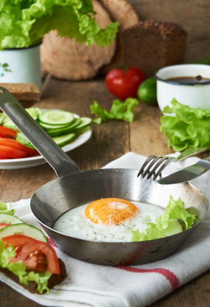 Ovo frito em uma frigideira com legumes em uma mesa de madeira