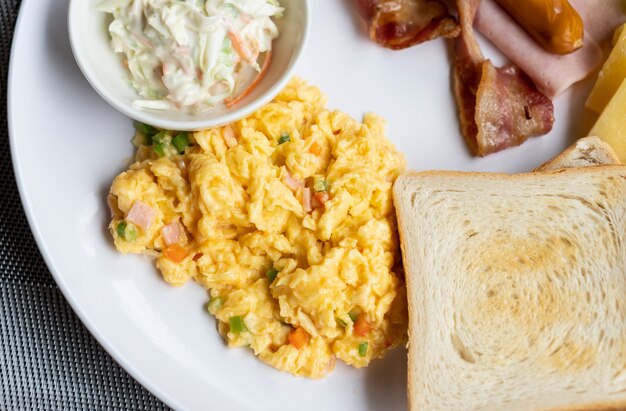 Ovo mexido com pão, salsicha, bacon e salada no prato branco, café da manhã simples do hotel comida saudável