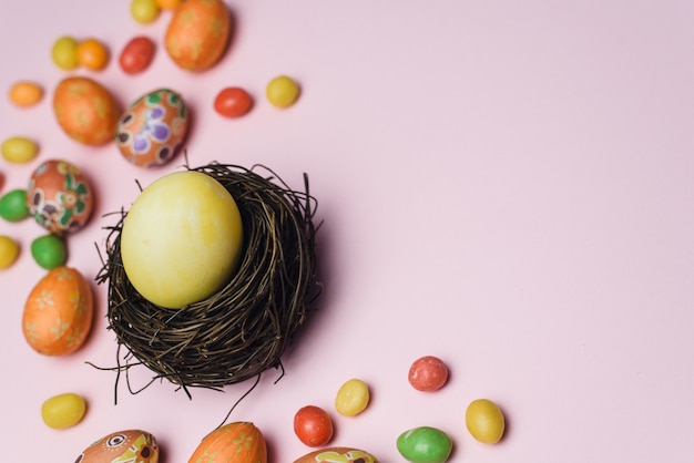 Ovo pintado de amarelo para o feriado da Páscoa em um ninho de galhos ao lado de doces
