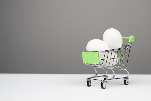 Ovos brancos de galinha em um carrinho de compras em um fundo cinza com espaço de cópia foto de alta qualidade