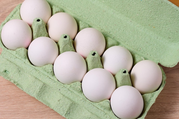 Ovos brancos inteiros frescos em embalagens de papel verde sobre uma mesa de madeira