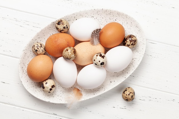 Ovos brancos marrons e de codorna em prato sobre fundo de madeira Vista superior Flat lay