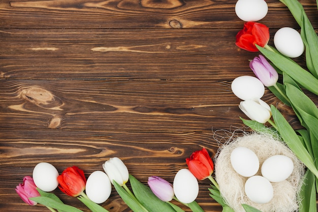 Foto ovos brancos no ninho com tulipas na mesa de madeira marrom