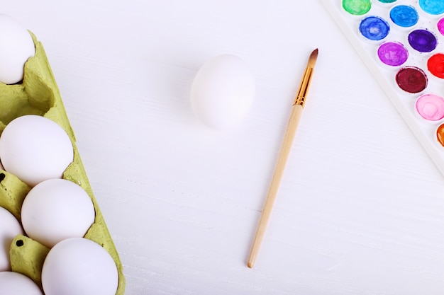 Ovos brancos, tintas e borlas, preparação para colorir para a Páscoa.