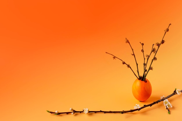 Ovos coloridos com grama verde primavera e galho de árvore florida em um fundo laranja Tradições familiares de férias de Páscoa