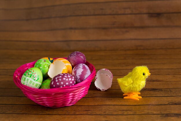 Ovos coloridos de páscoa na cesta e frango de brinquedo na mesa de madeira Decoração tradicional da religião