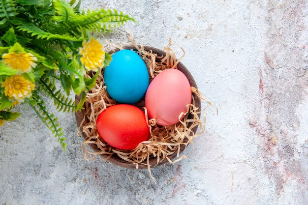 Ovos coloridos em um canudo em uma panela de madeira marrom e flores em um fundo de gelo com espaço livre