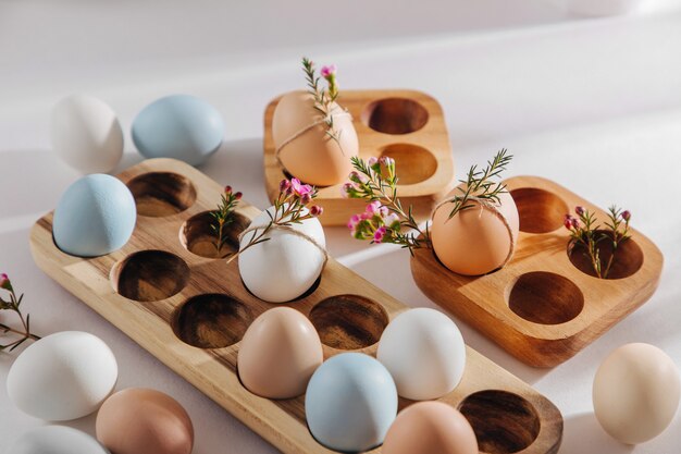 Ovos coloridos naturais em caixa de ovo de madeira e flores com luz solar. Composições elegantes em tons pastel. Conceito ecológico.