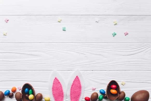 Foto ovos da páscoa do chocolate e orelhas de coelho no fundo de madeira branco.