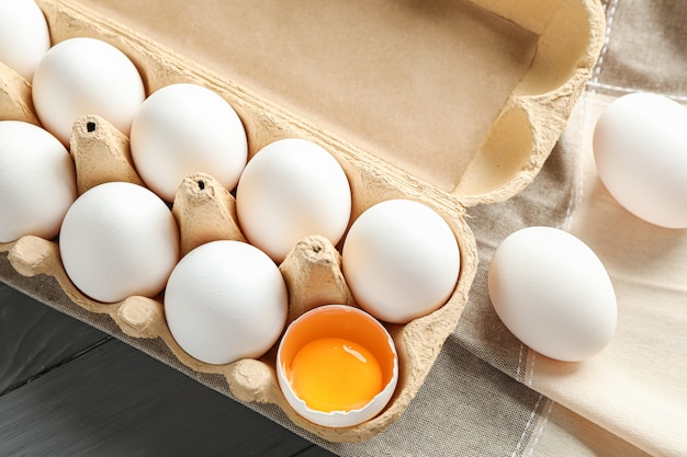 Ovos de galinha branca em caixa de papelão e toalha de cozinha na mesa de madeira