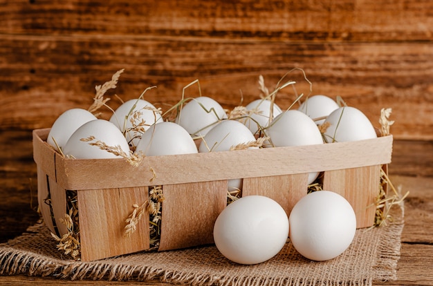 Ovos de galinha branca em um recipiente de madeira com feno. Copie o espaço.