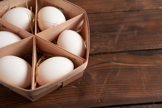 Ovos de galinha branca mentem na cesta de madeira redonda que fica em uma mesa de madeira escura. fundo de páscoa férias sazonais plana leigos com espaço livre para texto.