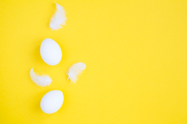 Ovos de galinha brancos e penas na superfície amarela. Copie o espaço.