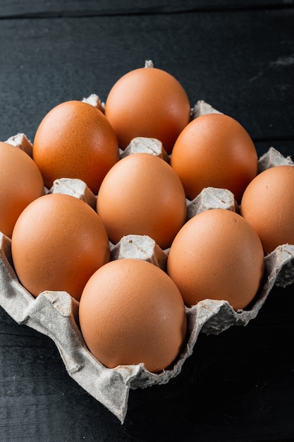 Ovos de galinha crus em caixa de ovo definida, no fundo preto da mesa de madeira