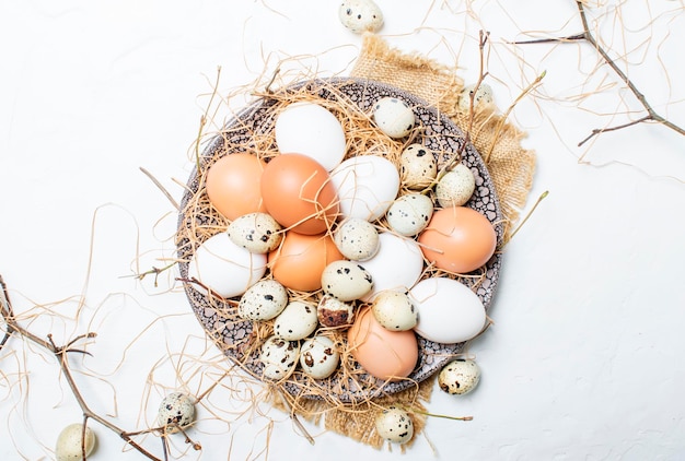 Ovos de galinha e codorna multicoloridos com palha e galhos primavera composição de páscoa vista superior