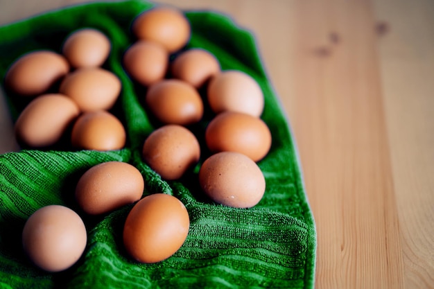 Ovos de galinha fresca marrom na toalha de cozinha verde na mesa de madeira. Conceito de produtos agrícolas, alimentos naturais, alimentação saudável, páscoa. Tiro vertical.