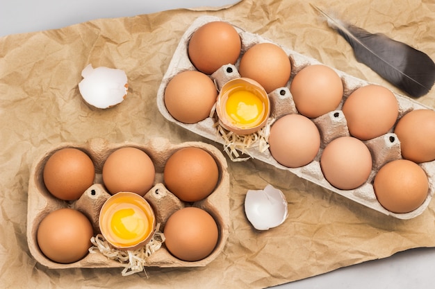 Ovos de galinha marrom em embalagem de papelão. ovos quebrados no recipiente. casca de ovo na mesa.