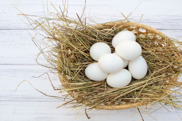 Ovos de galinha na cesta com feno em um fundo de madeira branca. ovos no feno