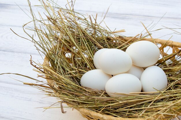 Ovos de galinha na cesta com feno em um fundo de madeira branca. ovos no feno