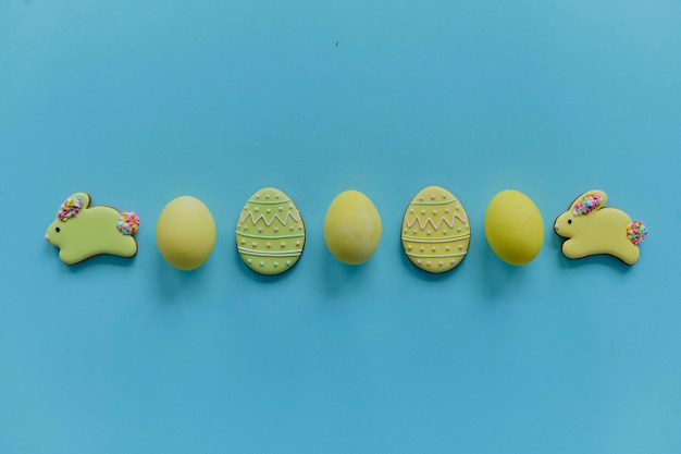 Ovos de galinha pintados de amarelo e biscoitos amarelos em forma de coelho e ovos em uma vista superior de fundo azul