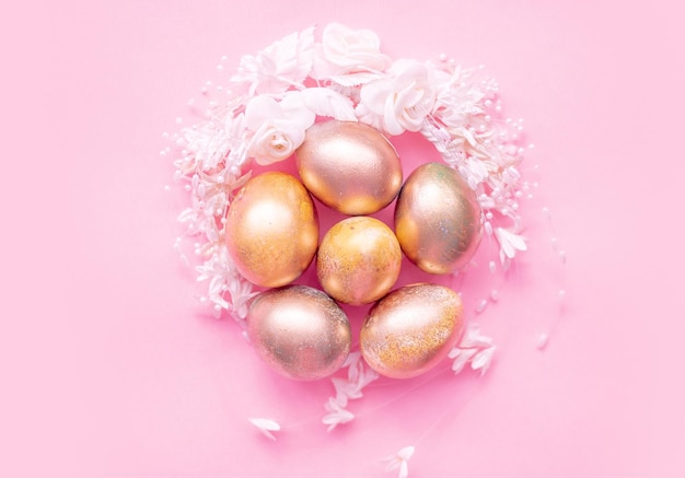 Ovos de ouro em um ninho de flores em um fundo rosa conceito de Páscoa com espaço para texto