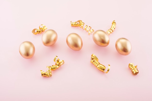 Ovos de ouro sobre fundo rosa, decorado com fitas de ouro. O conceito de Páscoa e o símbolo do feriado.