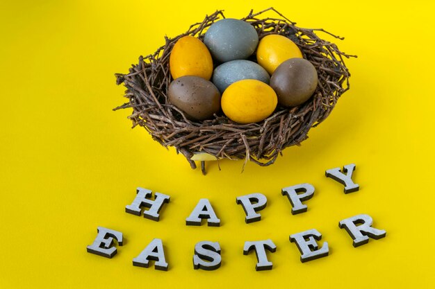 Ovos de páscoa amarelos azuis e marrons em pássaros nidificam em fundo amarelo Letras de feliz páscoa Vista superior