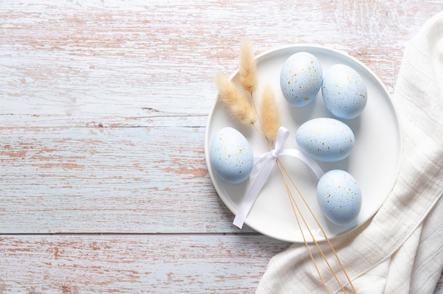 Foto ovos de páscoa azuis com manchas douradas e alguns espinhos em um prato branco com um guardanapo branco