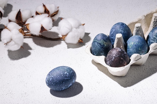Ovos de páscoa azuis tingidos com chá de hibisco em uma caixa de ovos em um fundo branco de concreto