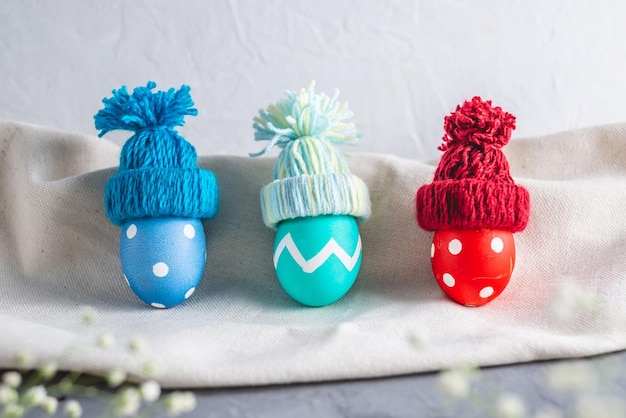 Ovos de páscoa coloridos brilhantes em chapéus de inverno de malha em um fundo cinza Cartão de páscoa de primavera festiva