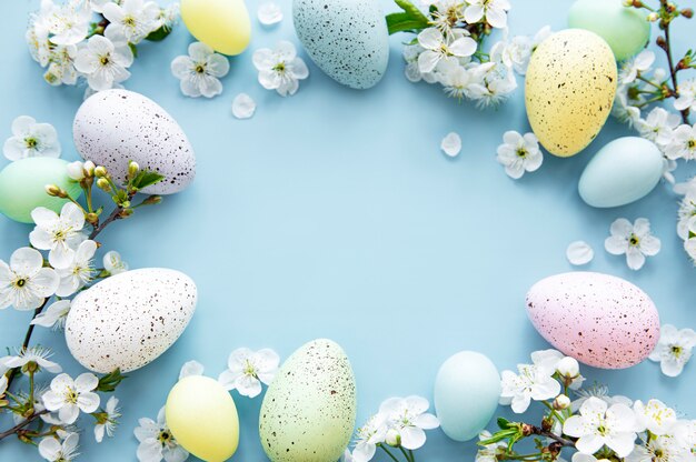 Ovos de páscoa coloridos com fundo azul de flores de flor de primavera. fronteira de férias de ovo colorido.