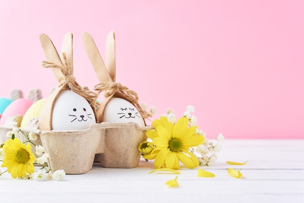 Ovos de Páscoa coloridos com rostos pintados na bandeja de papel com decoração em um fundo rosa