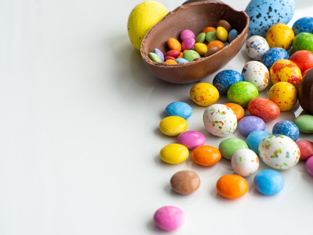 Ovos de páscoa coloridos e de chocolate com drageia doce em fundo branco