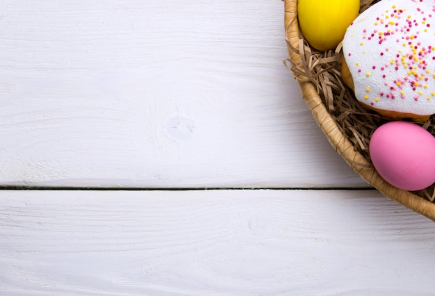 Ovos de Páscoa coloridos e pouco bolo de Páscoa no ninho beasket em branco de madeira superfície superior branco