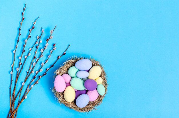 Ovos de páscoa coloridos em um ninho decorativo de ramos de palha e salgueiro sobre um fundo azul, cópia espaço, configuração plana