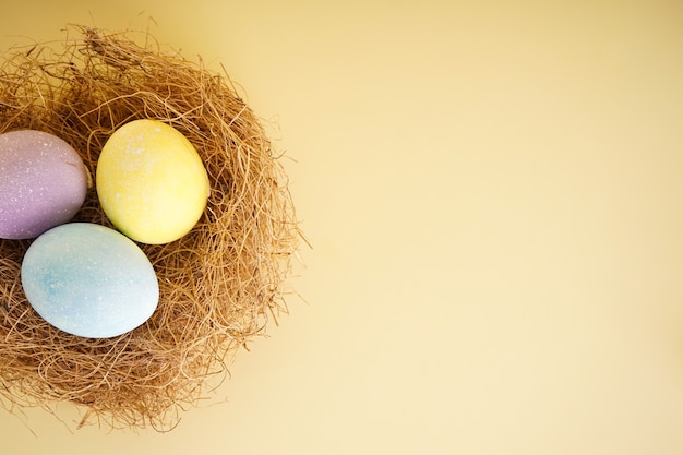 Ovos de Páscoa coloridos em um ninho em um fundo amarelo com espaço de cópia