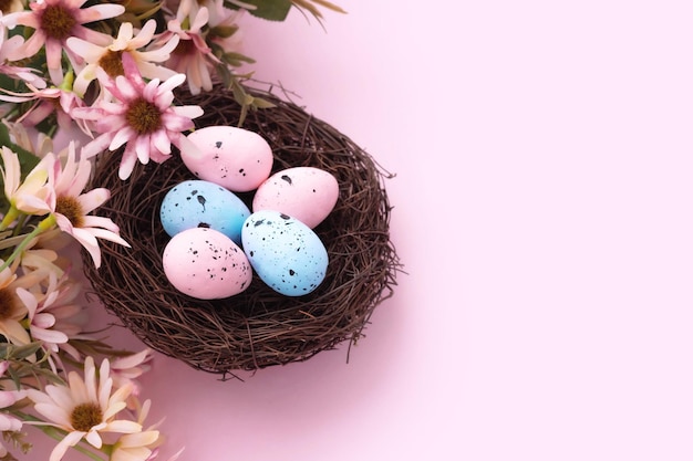 Ovos de Páscoa coloridos no ninho e flores sobre fundo rosa com espaço de cópia. Postura plana.