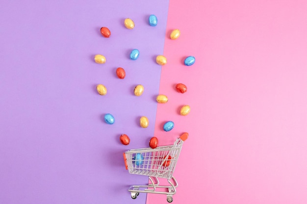 Foto ovos de páscoa de chocolate derramados de um carrinho de compras em um fundo rosa lila
