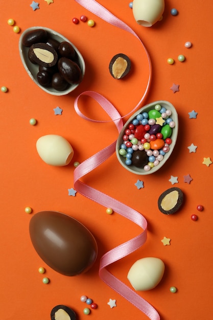 Ovos de Páscoa de chocolate, doces e granulado na superfície laranja