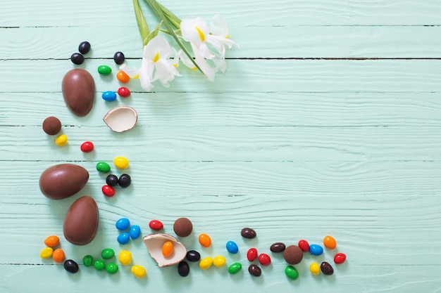 Ovos de páscoa de chocolate e flores em superfície de madeira verde