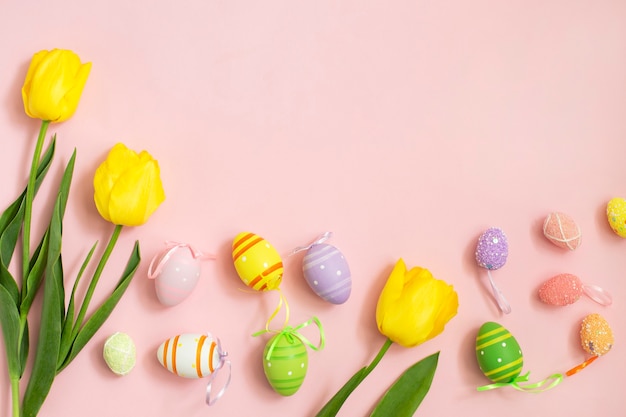 Ovos de páscoa de cor e tulipas amarelas brancas em um fundo rosa.