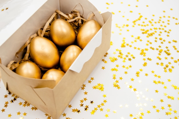 Ovos de Páscoa de ouro em uma caixa com estrelas douradas sobre fundo branco