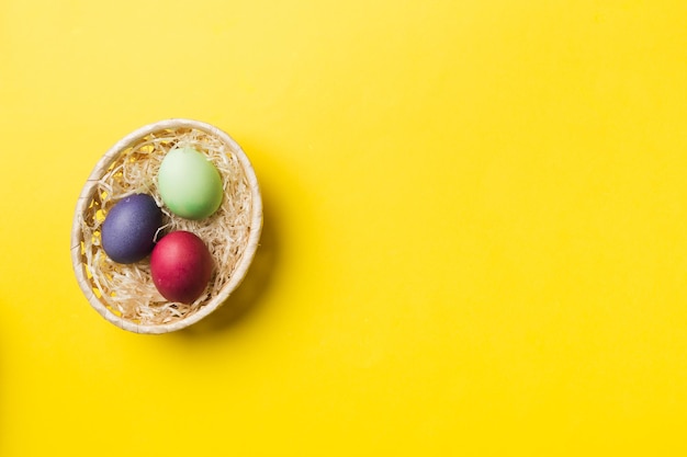 Ovos de páscoa de várias cores na cesta tecida em fundo colorido Conceito de férias de ovos de páscoa de cor pastel com espaço de cópia