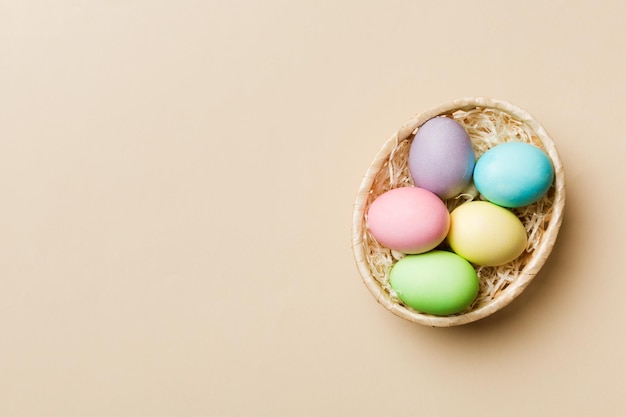 Ovos de páscoa de várias cores na cesta tecida em fundo colorido Conceito de férias de ovos de páscoa de cor pastel com espaço de cópia
