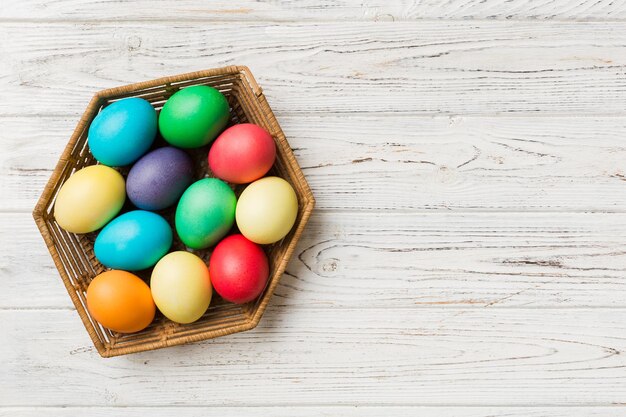 Ovos de páscoa de várias cores na cesta tecida em fundo colorido Conceito de férias de ovos de páscoa de cor pastel com espaço de cópia